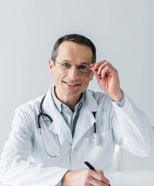 Smiling MMJ doctor with glasses, writing on a notepad - TeleLeaf